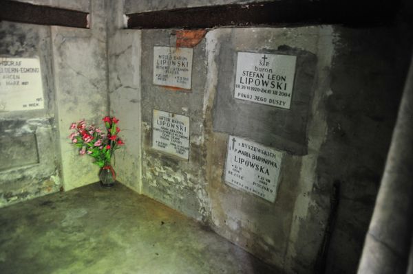 Wnętrze grobowca Lipowskich w Hucisku: tablice nagrobne członków rodziny w betonowych ścianach, w rogu wazon z czerwonymi kwiatami.
